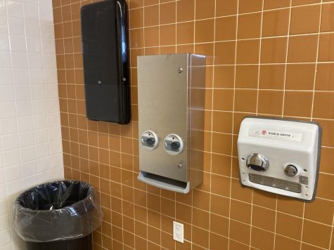 The empty paper towel dispenser next to the air dryer in the B building bathroom.