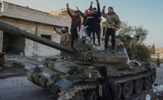 Syrian opposition supporters stand on top of a captured army tank in a town near Aleppo